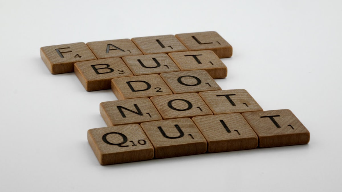 Wooden Scrabble tiles arranged to spell 'Fail but do not quit,' inspiring determination.